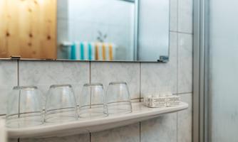 A modern bathroom with a mirror and four glasses on a shelf. Towels are visible in the background.