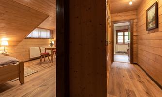 A cozy room with wooden walls and warm lighting. In the background, another room can be seen, furnished with a table and chairs.