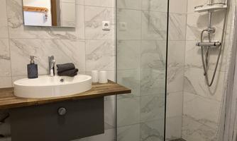 A modern bathroom with a glass shower and an elegant sink. The walls are decorated with light, marbled tiles.