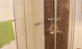 A modern shower with glass walls and a simple design. The bathroom has bright tiles and a green towel rack.