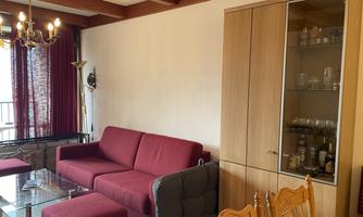 A modern living room with a red sofa and a glass table. In the background, there is a wooden cabinet with glasses.