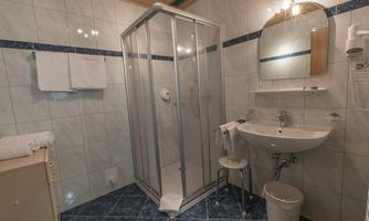 A modern bathroom with a glass cabin and a shower. There is a sink, towels, and a small seating area.