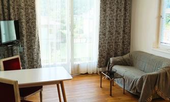 A bright living space with a table, two chairs, and a sofa. Large windows let in plenty of light and provide a view outside.