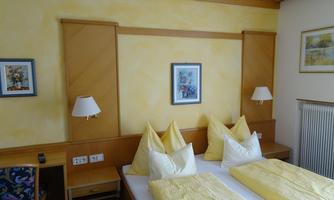 A cozy bedroom with two beds and yellow pillows. Pictures hang on the walls, and there are bedside lamps.