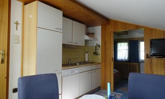 A cozy kitchen with wooden shelves and white cabinets. In the background, a table and a seating area can be seen.