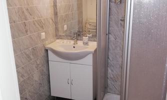 A modern bathroom with a sink and a shower cubicle. Walls with gray tiles and bright lighting create a friendly atmosphere.
