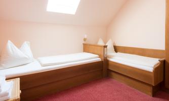 A simple, bright room with two beds and a window. The walls are painted in a soft, neutral color.