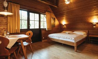 A cozy room with wooden paneling, a large window, and a double bed. There is a table with chairs and warm light from the wall sconces.