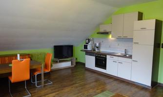 A modern kitchen with a dining area and a television. The walls are painted in a fresh shade of green.