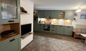 A modern kitchen with green cabinets and wooden details. The room is well-lit and provides space for a dining group.