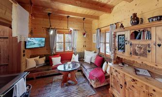 A cozy wooden cabin with warm colors and an inviting living room. There is a sofa, a table, and a wooden shelf with decoration.
