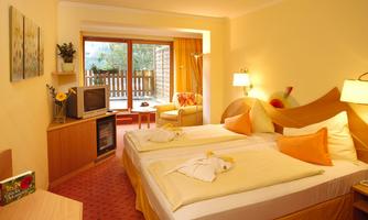 A cozy bedroom with two beds, a television, and a balcony. The colors are warm and inviting, with orange accents.