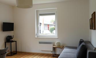 A modern living room with a gray sofa and a table. The room has wooden floors and a window that lets in a lot of light.