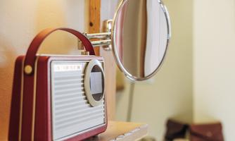 A red radio is on a shelf next to a round mirror. In the background, glasses and a bag can be seen.