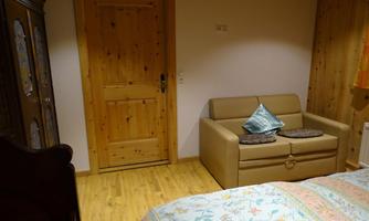 A cozy room with a comfortable sofa and a single bed. The walls are made of wood and the decor is rustic.