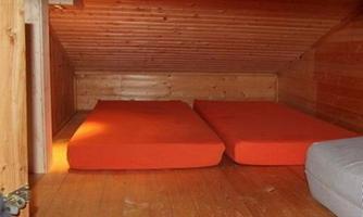 A cozy room with two orange mattresses on a wooden floor. The walls are made of wood and the ceiling is slanted.