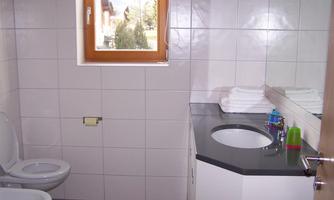 A modern bathroom with a sink and a toilet. There are towels and a large mirror, as well as plenty of daylight coming through the window.