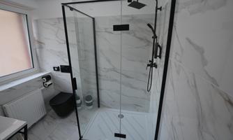 A modern shower with glass partition in a bright bathroom. The walls are clad with elegant marble tiles.
