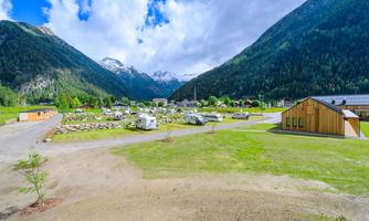 A beautiful campsite in the mountains with motorhomes and green meadows. In the background, tall mountains and a blue sky can be seen.