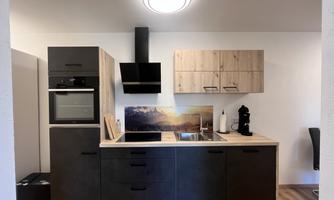 A modern kitchen with wood and black elements. It features a cooking area, an oven, and a range hood.