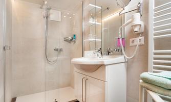 A modern bathroom with a glass shower and a sink. Towels and personal care products are placed on the shelf.