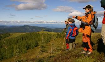 A group of children is standing on a hill and looking into the distance. They are wearing colorful hiking clothes and are surrounded by a beautiful landscape.