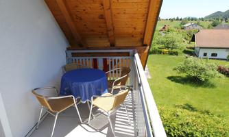 A cozy balcony with a round table and four chairs. In the background, there is a green landscape with trees and houses.