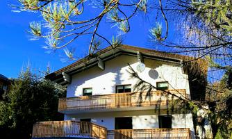 A modern house with a large balcony and a clear blue sky. Surrounded by green trees, it offers an inviting atmosphere.
