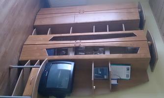 A living room with modern wooden cabinets and an old television. The furniture is functional and well-arranged.