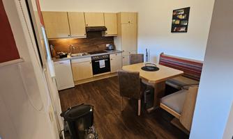 A modern kitchen with wooden furniture and a dining table. The surroundings are well-lit and cozily designed.