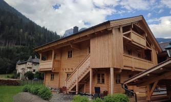 A cozy wooden house in a picturesque mountain landscape. Green meadows and trees surround the building as clouds pass by in the sky.