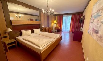 A cozy bedroom with a large bed and modern furnishings. The room has large windows with curtains and pleasant lighting.