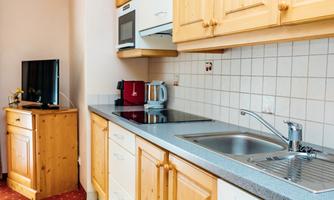 A modern kitchen with wooden cabinets and a bright, friendly atmosphere. The kitchen equipment includes a stove, a refrigerator, and a sink.