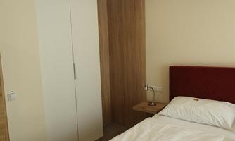 A simple bedroom with a single bed and a red headboard. On the wall, there is a bright wardrobe and a bedside table with a lamp.