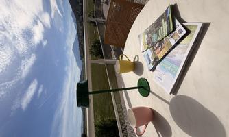 A balcony with a table, two cups, and a green lamp. In the background, mountains and a blue sky are visible.