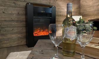 A cozy room with an electric fireplace and wooden paneling. On a table are a bottle of white wine and two wine glasses.