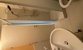 A small bathroom with a shower, a sink, and a toilet. The walls are light-colored and the room feels clean and modern.
