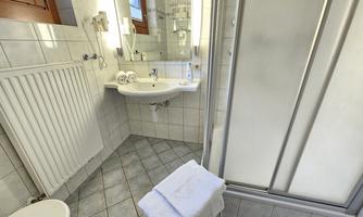 A modern bathroom with a shower, sink, and toilet. The walls are tiled and there are large windows that let in a lot of light.