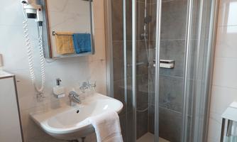 A modern bathroom with a shower cabin and a sink. There are towels and a mirror arrangement.