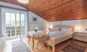 A cozy bedroom with a sloping roof and wooden elements. There is a double bed, a table, and a beautiful view from the window.