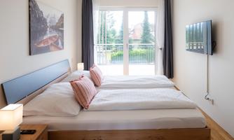 A modern bedroom with two beds and cozy pillows. Large windows provide plenty of daylight and offer a view outside.