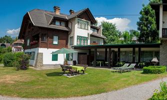 A cozy house with a large garden and a terrace. Surrounded by trees and a clear, blue sky.