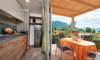 A cozy kitchen area with modern furniture and an outdoor table. The view shows the surrounding mountains and a green landscape.
