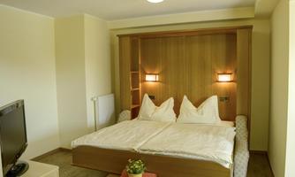 A cozy bedroom with a double bed and soft wall lamps. The room has a bright, inviting atmosphere and a television in the corner.