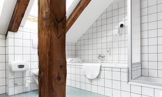A modern bathroom with white tiles and a wooden supporting beam. It features a bathtub, a shower, and fresh towels.