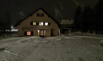 A house in the snow at night, with lit windows. The surroundings are calm and wintry.