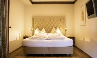 A cozy bedroom with a large double bed and soft colors. The walls are light, and a television is mounted on the wall.