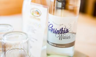 A bottle of Carinthia water is standing on a table. Next to it are glasses and an information sheet.