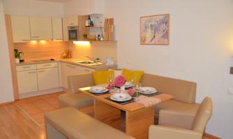 A cozy living kitchen with a dining table and comfortable seating. Decorative plates and flowers are arranged on the table.