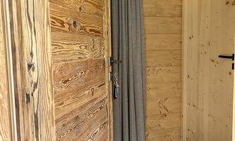 An inviting entrance door made of wood with a soft curtain and a modern lamp. The floor is designed with tiles and rugs.